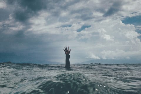 Offenes Meer mit Wellen ist zu sehen. Ein Arm guckt hilfesuchend heraus. Im Hintergrund sind ganz schwach Berge zu erkennen.