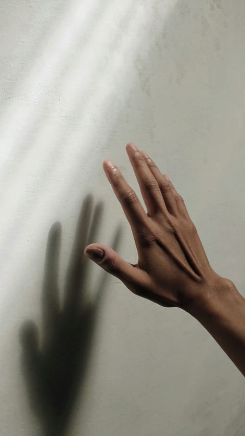 Ein Hand und ihr schatten vor einer Wand, sie wirkt suchend.