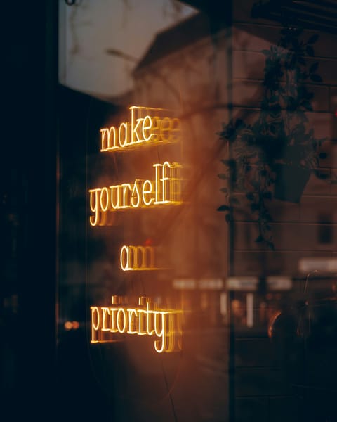 Ein bild durch eine Glasscheibe Fotografiert wohinter ein Leuchtschild ist was sagt „make yourself a priority“