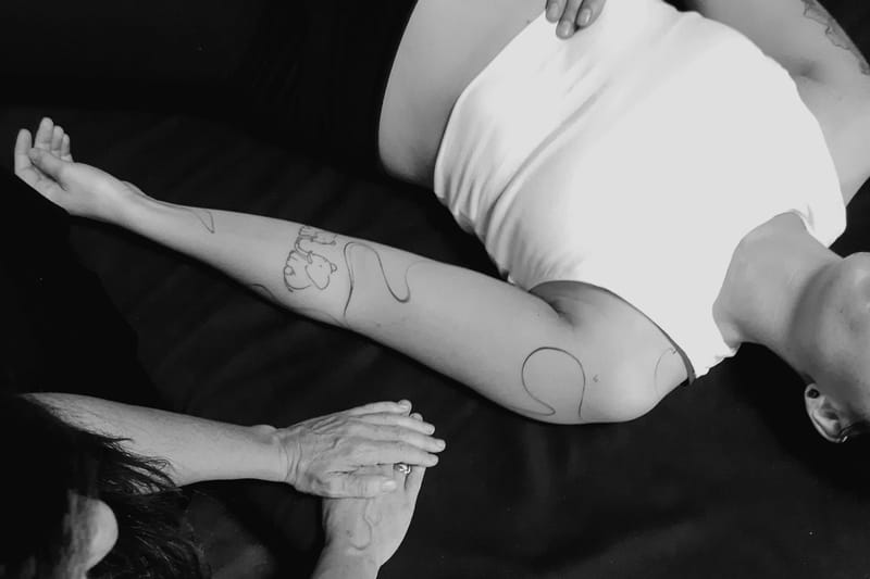 Eine Frau liegt auf einer Matte und Atmet. Daneben sind Hände von dem Practitioner zu sehen die neben der Frau auf der Matte liegen und für sie da sind.