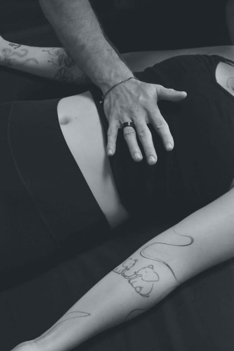 Ein Oberkörper von einer Frau die liegt und Atmet, auf ihrem Zwerchfell liegt eine Hand die sie begleitet und unterstützt.