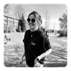 Eine Frau, lachend mit Sonnenbrille und Tshirt an. Steht in der Natur.