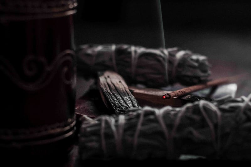 ein dunkles Bild wo Salbei und Palo Santo zu sehen ist. Es brennt ein Räucherstäbchen.